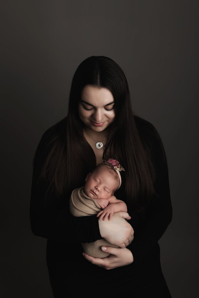 Photographe naissance dans les Yvelines – maman tenant son nouveau-né emmailloté dans une ambiance douce