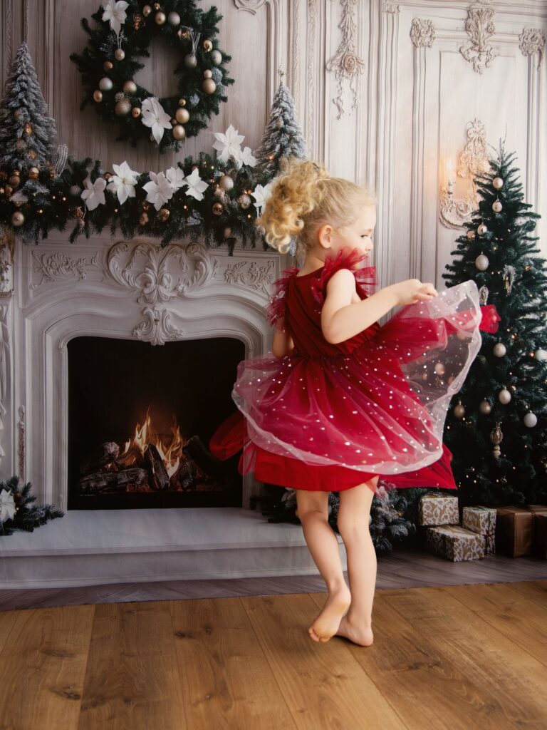 Une petite fille fait tournoyer sa robe rouge devant une cheminée ornée de décorations de Noël.
