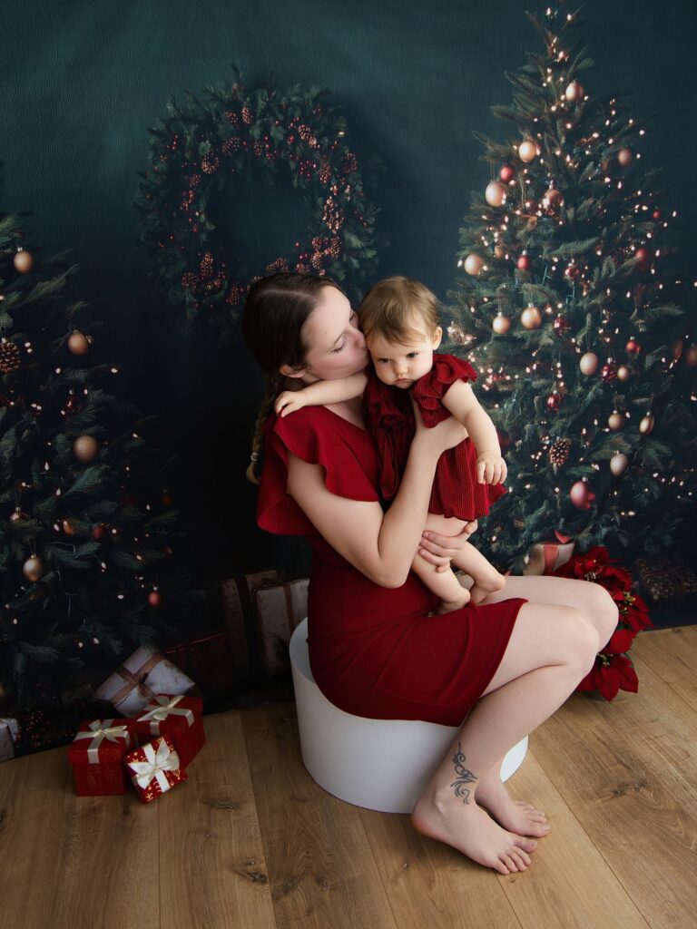 Une maman assise avec ses deux filles en tenue rouge au milieu des sapins décorés pour Noël au studio Rose Basile.