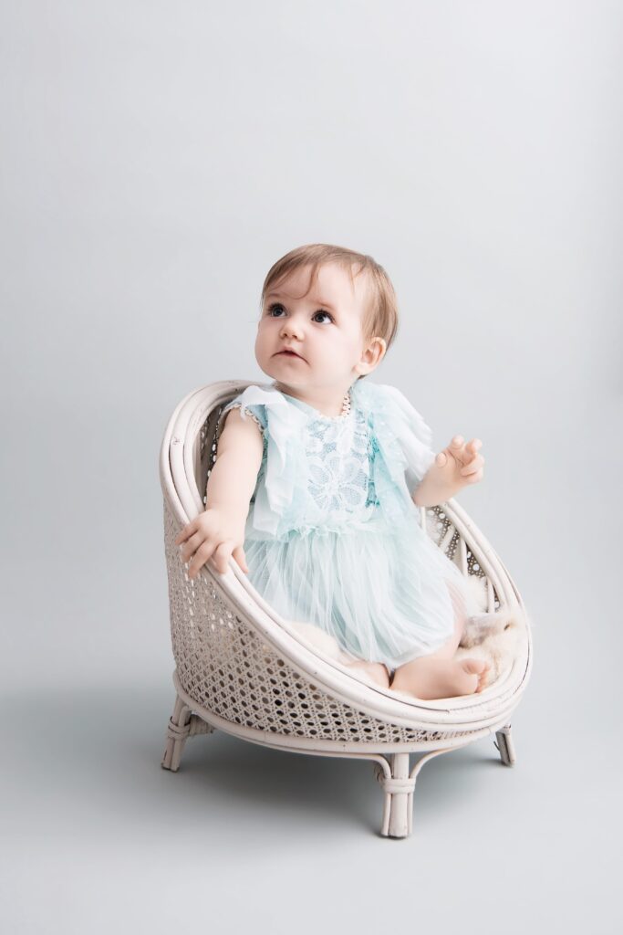 Bébé assise, en robe bleue, sur fond bleu