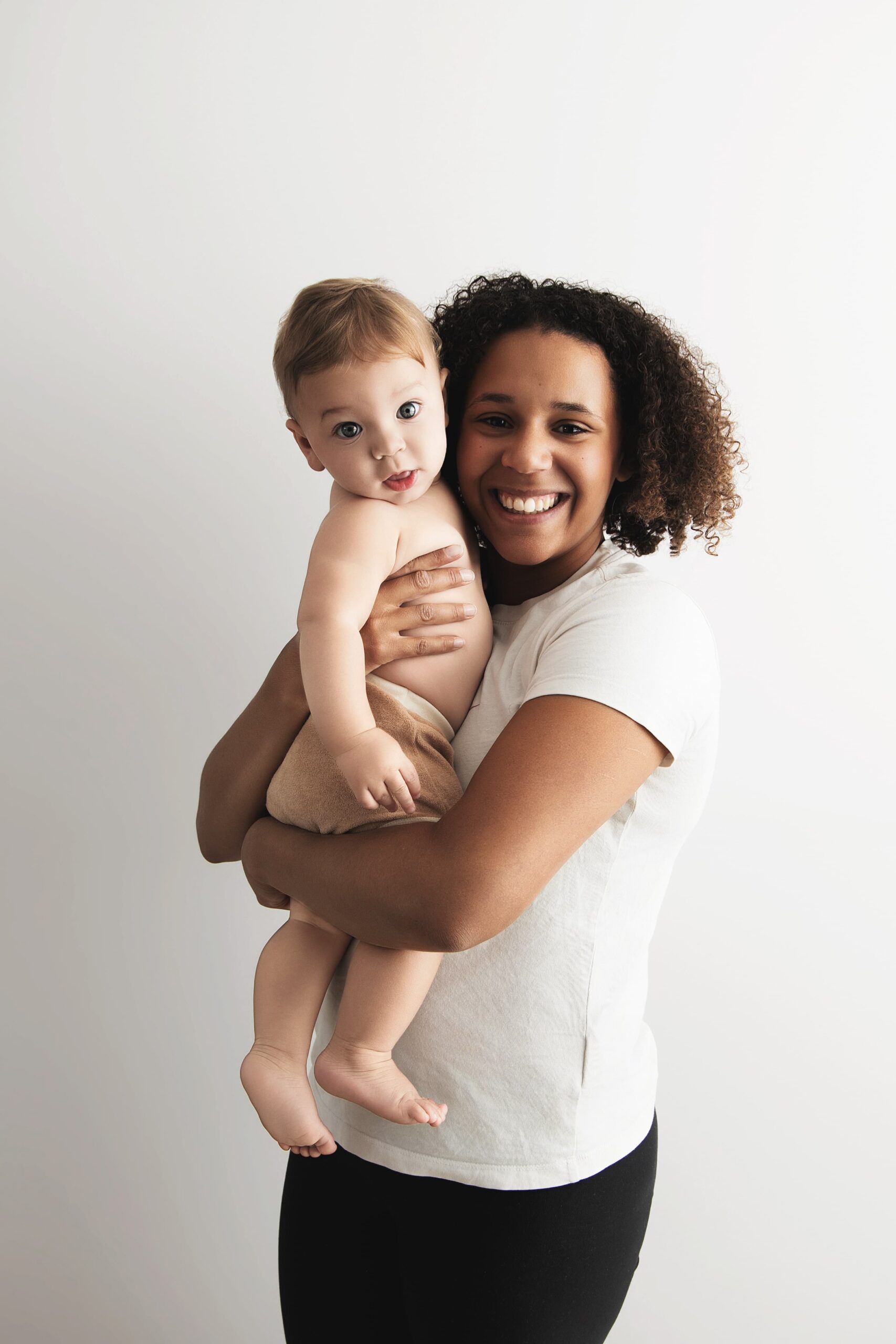 Maman qui éclate de rire en tenant son bébé de 8 mois contre elle, séance Les Liens en studio à Juziers
