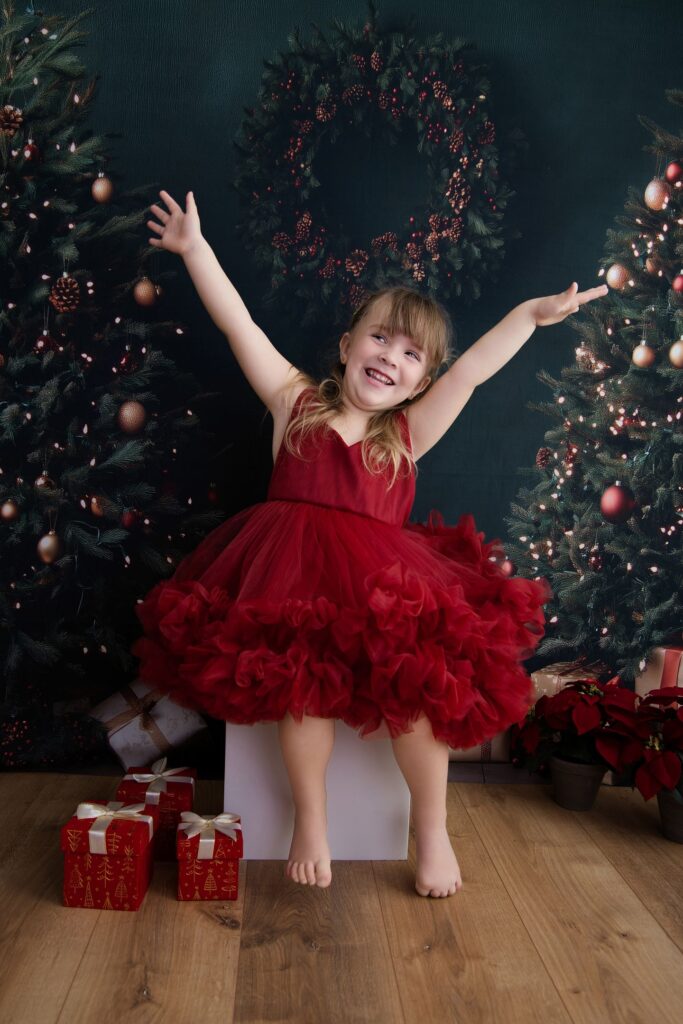 Fille de trois ans en robe rouge devant les sapins de Noël