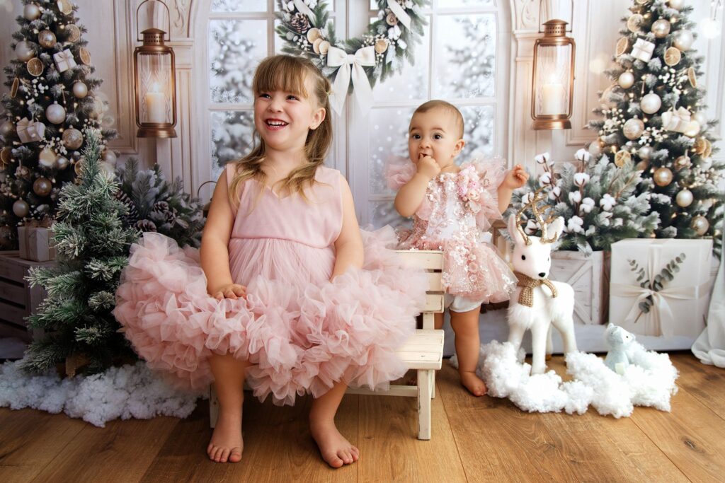 Deux sœurs en robes de tulle rose, debout devant une arche blanche et une fenêtre enneigée